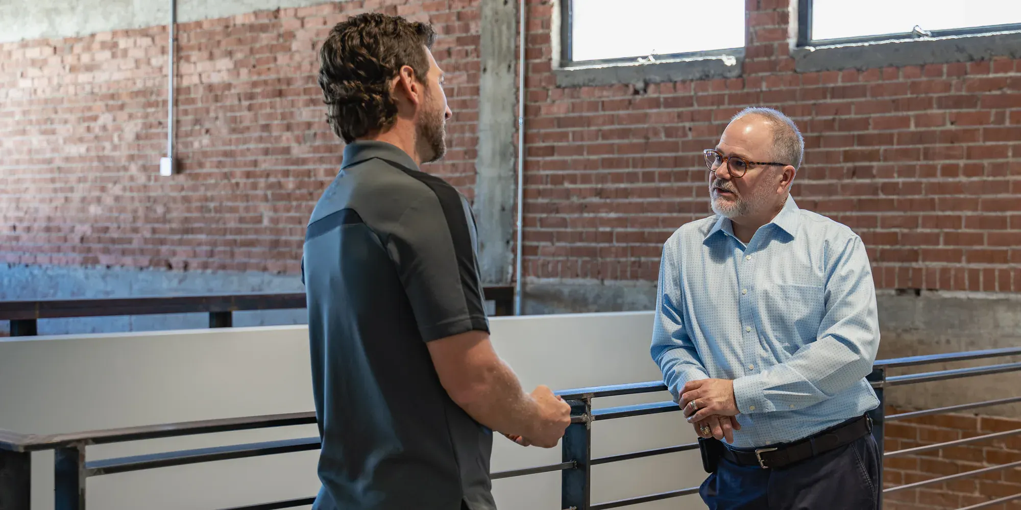 Two people talking beside a rail in an open workspace
